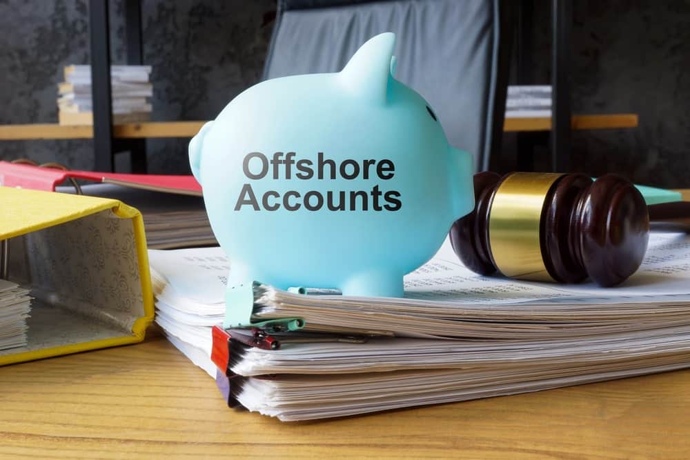 Image is of a piggy bank labeled offshore accounts placed on financial documents and legal files, concept of how asset searches identify indicators of hidden or offshore assets