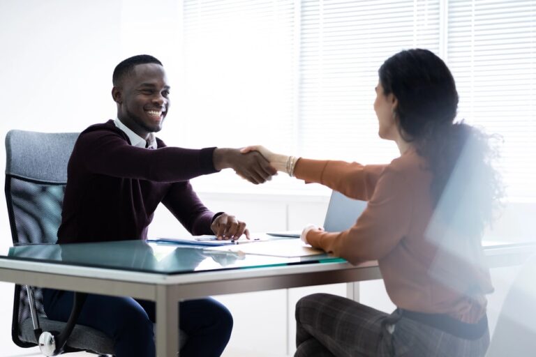Image is of an employer and job applicant shaking hands during an interview, concept of how credit reports may be reviewed during hiring decisions.