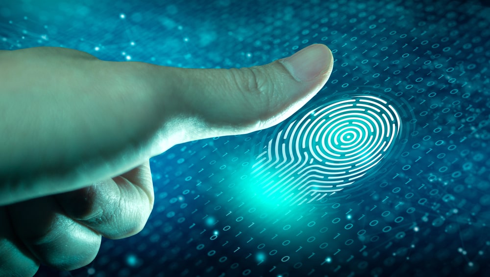 Image is of a person pressing a finger onto a digital scanner, representing fingerprint checks used during background screening and verification procedures.